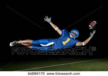 Stock Image - Mixed race football player jumping in mid-air catching football. Fotosearch