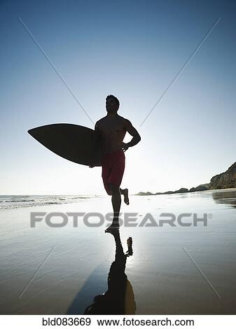 Mixed race man carrying surfboard on beach View Large Photo Image Stock Photo - Mixed race man carrying surfboard on beach. Fotosearch
