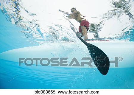 Stock Photography - Mixed race man paddling on surfboard. Fotosearch