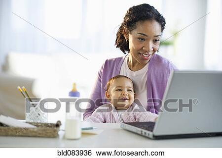 Mixed race woman holding baby and using laptop View Large Photo Image Stock Photograph - Mixed race woman holding baby and using laptop. Fotosearch