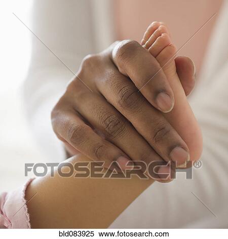 Stock Photography - Mixed race woman holding baby's foot. Fotosearch