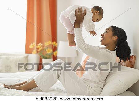 Stock Image - Mixed race woman lifting baby. Fotosearch