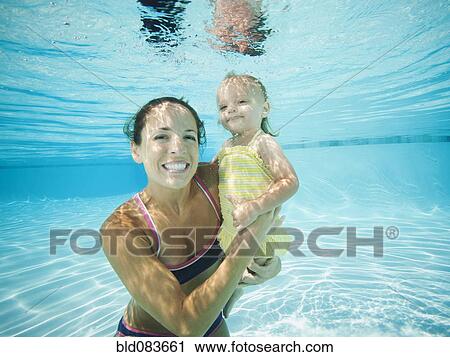 Stock Image - Mother underwater in swimming pool with daughter. Fotosearch
