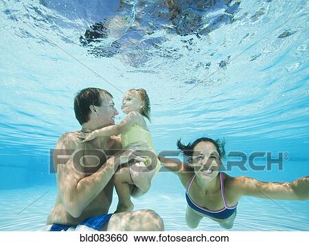 Stock Image - Parents swimming in swimming pool with daughter. Fotosearch