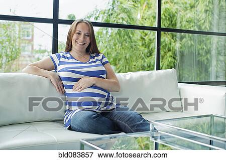 Pregnant Caucasian woman sitting on sofa View Large Photo Image Stock Photo - Pregnant Caucasian woman sitting on sofa. Fotosearch