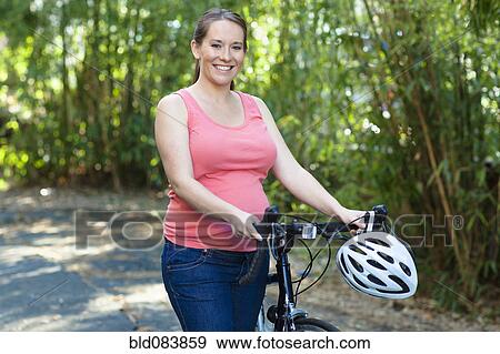 Stock Photo - Pregnant Caucasian woman standing with bicycle. Fotosearch