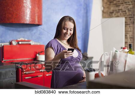 Pregnant Caucasian woman text messaging in kitchen View Large Photo Image Stock Image - Pregnant Caucasian woman text messaging in kitchen. Fotosearch