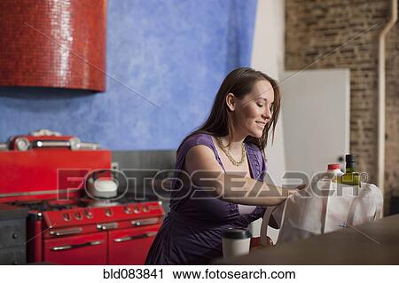 Stock Image - Pregnant Caucasian woman unpacking groceries in kitchen. Fotosearch