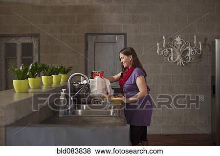 Stock Photo - Pregnant Caucasian woman with groceries in kitchen. Fotosearch