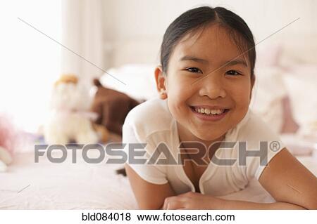 Stock Photo - Smiling Asian girl laying on bed. Fotosearch