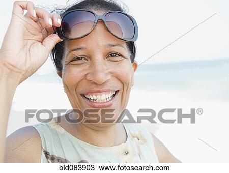 Stock Image - Smiling Black woman wearing sunglasses on beach. Fotosearch