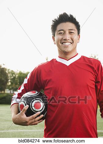Picture - Asian soccer player holding ball on soccer field. Fotosearch