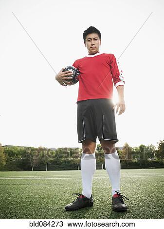 Stock Image - Asian soccer player holding ball on soccer field. Fotosearch