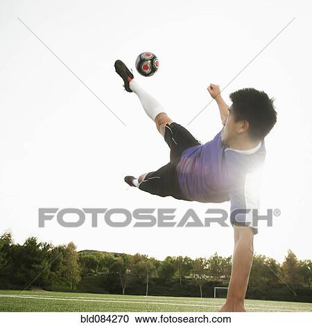 Stock Image - Asian soccer player in mid-air kicking soccer ball. Fotosearch