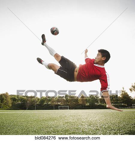 Stock Photograph - Asian soccer player in mid-air kicking soccer ball. Fotosearch
