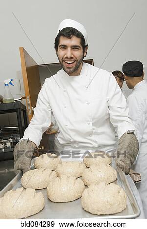 Stock Photo - Baker carrying tray of bread dough in bakery kitchen. Fotosearch
