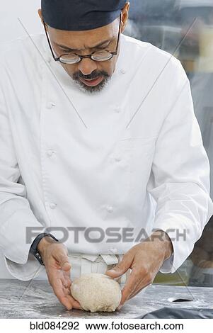 Stock Image - Baker working with dough in bakery kitchen. Fotosearch
