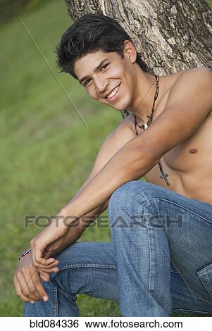 Stock Photograph - Bare chested Hispanic man leaning against tree. Fotosearch