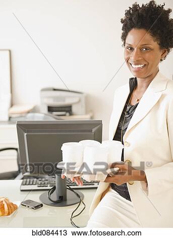 Stock Image - Black businesswoman carrying tray of coffees. Fotosearch