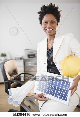Stock Photograph - Black businesswoman holding solar panel. Fotosearch