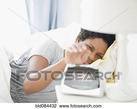Stock Image - Black woman turning off morning alarm. Fotosearch