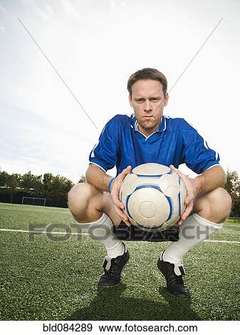 Stock Photo - Caucasian soccer player crouching holding soccer ball. Fotosearch