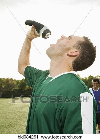 Stock Image - Caucasian soccer player drinking water on soccer field. Fotosearch