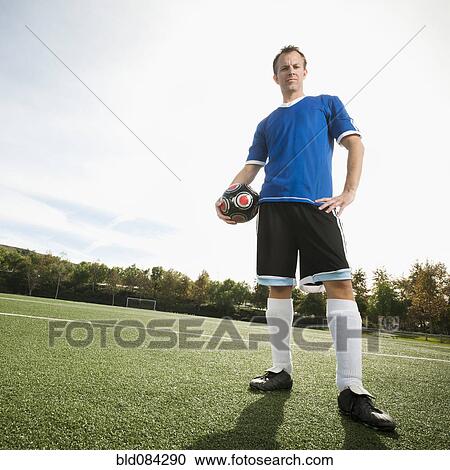 Stock Image - Caucasian soccer player holding ball on soccer field. Fotosearch