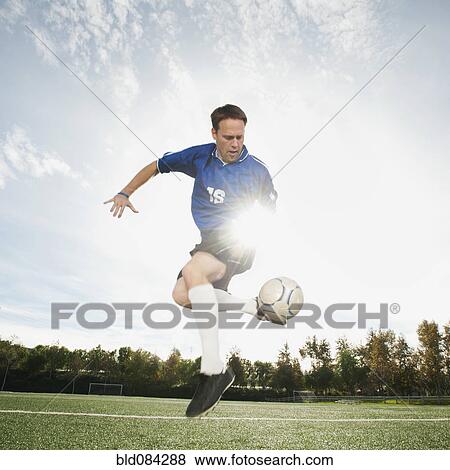 Stock Photo - Caucasian soccer player kicking soccer ball. Fotosearch
