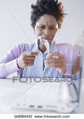 Stock Image - Confused Black woman looking at USB cables. Fotosearch
