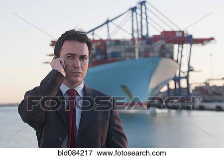 Hispanic businessman talking on cell phone with container ship in background View Large Photo Image Stock Photo - Hispanic businessman talking on cell phone with container ship in background. Fotosearch