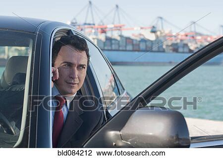 Hispanic businessman using cell phone in car with container ship in background View Large Photo Image Stock Image - Hispanic businessman using cell phone in car with container ship in background. Fotosearch