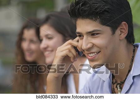 Hispanic man talking on cell phone with friends in background View Large Photo Image Stock Image - Hispanic man talking on cell phone with friends in background. Fotosearch