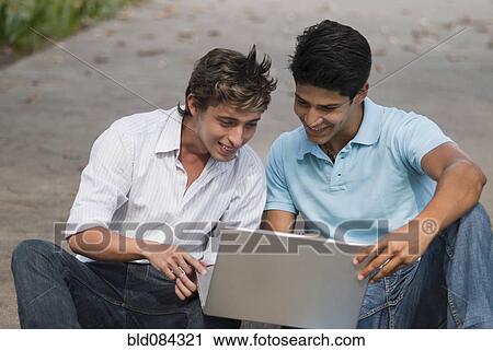 Stock Image - Hispanic men using laptop outdoors. Fotosearch