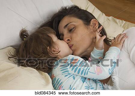 Stock Photography - Hispanic mother kissing daughter in bed. Fotosearch