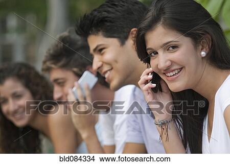 Picture - Hispanic woman talking on cell phone with friends in background. Fotosearch