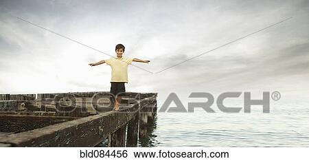 Stock Photograph - Mixed race boy walking on dilapidated pier. Fotosearch