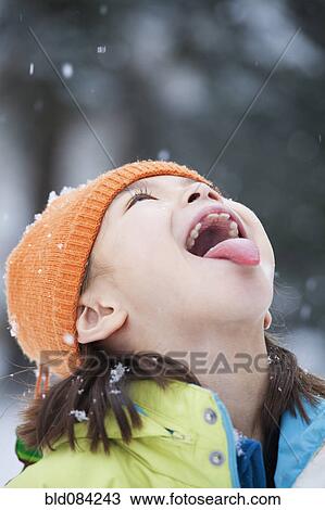 Stock Image - Mixed race girl catching snowflakes on tongue. Fotosearch