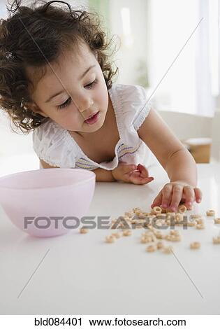 Stock Image - Mixed race girl picking up spilled cereal. Fotosearch