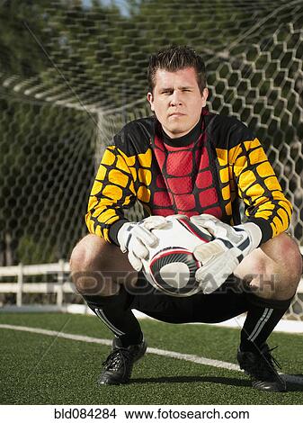 Picture - Mixed race goalkeeper crouching with soccer ball. Fotosearch