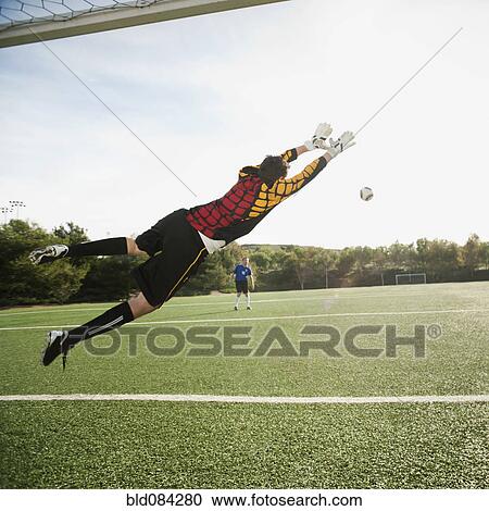 Stock Image - Mixed race goalkeeper in mid-air protecting goal. Fotosearch