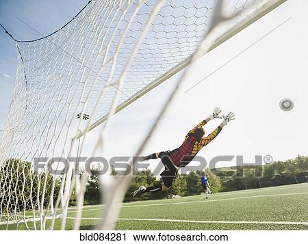 Stock Image - Mixed race goalkeeper in mid-air protecting goal. Fotosearch