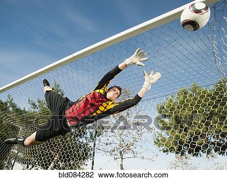 Stock Image - Mixed race goalkeeper in mid-air protecting goal. Fotosearch