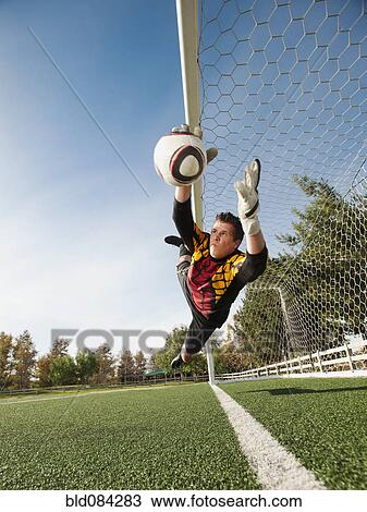 Stock Image - Mixed race goalkeeper in mid-air protecting goal. Fotosearch