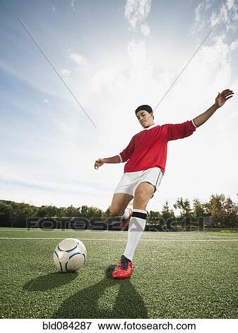 Stock Photo - Mixed race soccer player kicking soccer ball. Fotosearch