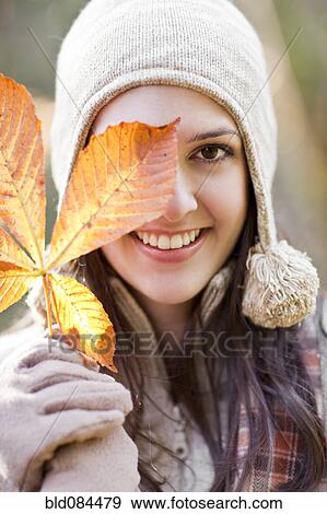 Mixed race woman in cap holding autumn leaf View Large Photo Image Stock Photo - Mixed race woman in cap holding autumn leaf. Fotosearch