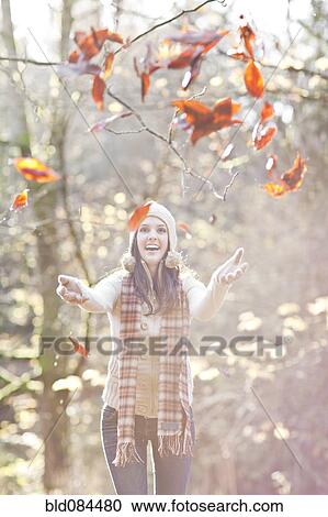 Stock Image - Mixed race woman in cap playing in autumn leaves. Fotosearch