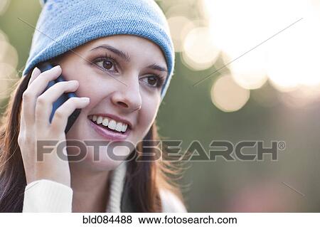 Stock Photo - Mixed race woman in cap talking on cell phone. Fotosearch
