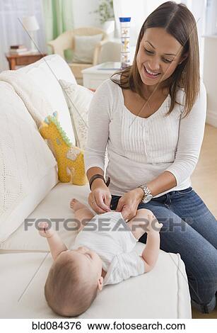Stock Photograph - Mother changing baby's diaper on sofa. Fotosearch