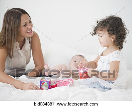 Stock Photo - Mother having tea party on bed with daughters. Fotosearch